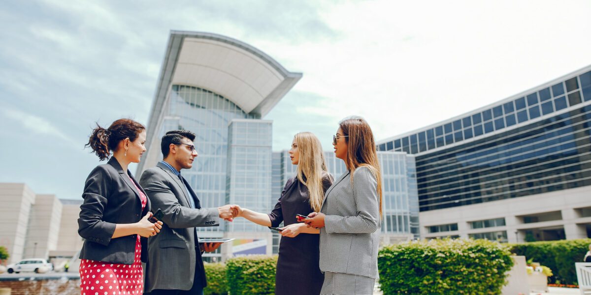 Handsome businessman in a city. Businessman in a glasses. Business partners in a summer city. Man and three women standingin a sity with tablet and phones